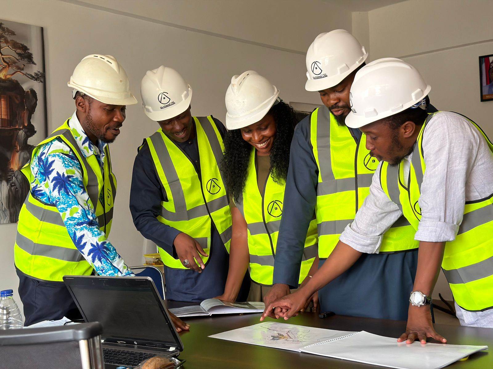 Group of engineers in hard hats and safety vests reviewing blueprints in an office setting
